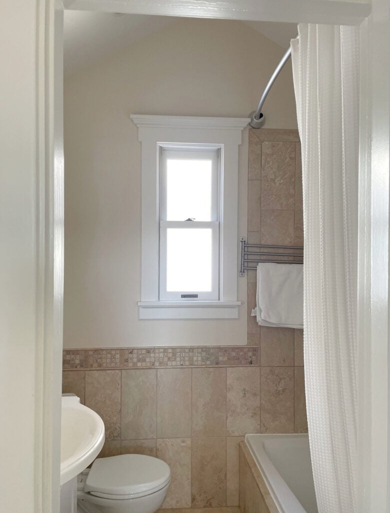 Sherwin Williams warm off-white beige walls with travertine tile bathroopm floor and shower surround. Pure White trim.