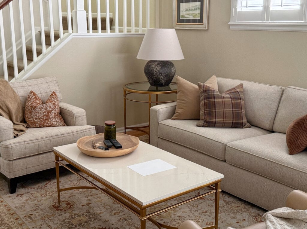 Beige sofa and chair in a living room with Benjamin Moore Carrington BEige walls, coffee table and table lamp. Homey