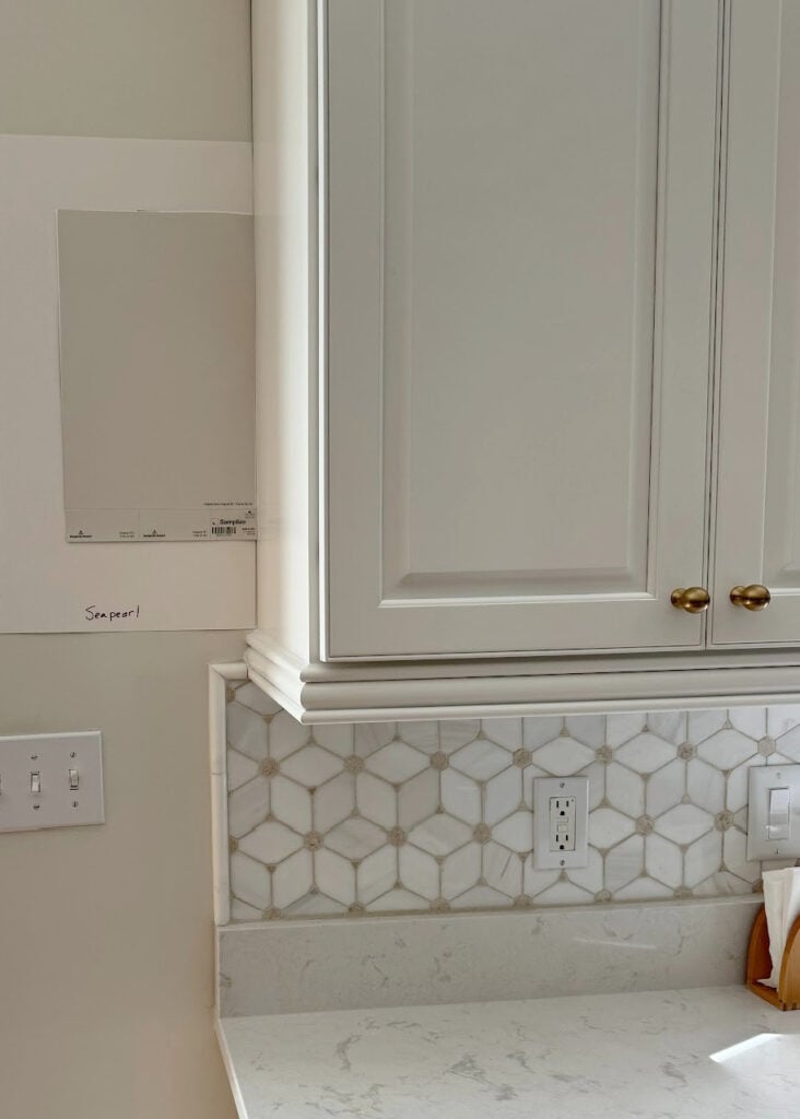 Benjamin Moore Sea Pearl paint color sample with off-white quartz and warm white kitchen cabinets, warm marble backsplash with beige details