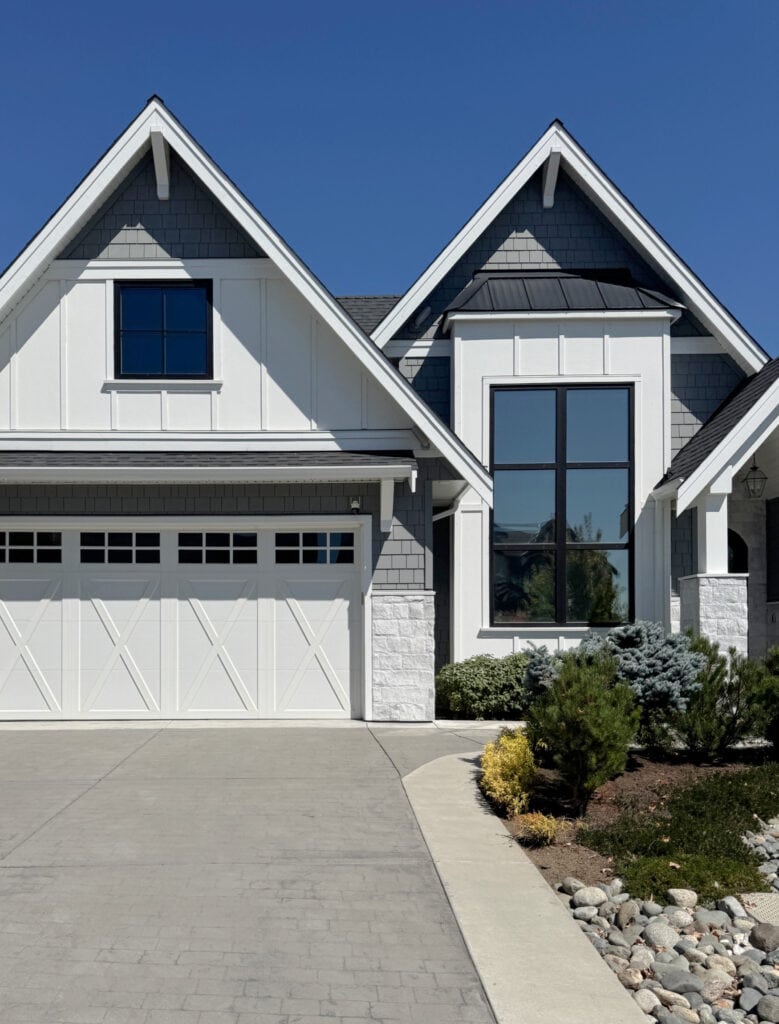 James Hardie Arctic White board and batten exterior siding, white trim, gray shakes in the peaks, black windows with gray stone in fuill sunshine