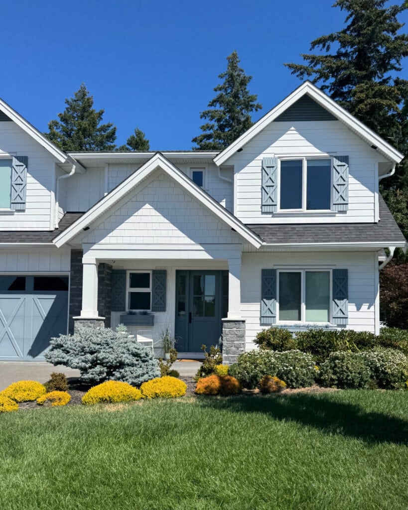 James Hardie Arctic White on home with gables and blue shutters, garage door, and front door. Gray stone, in full sunshine