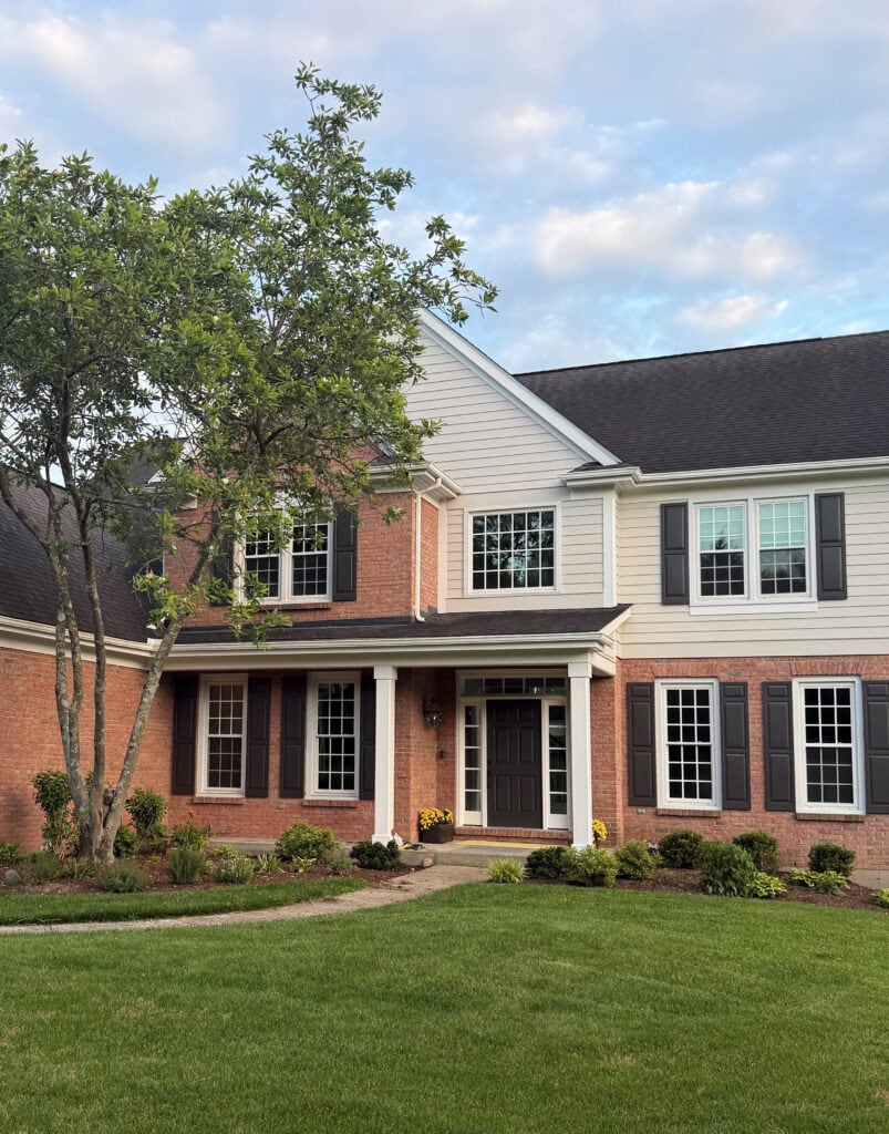 North-facing exterior with red-orange, pink brick, siding, and dark roof. Shutters. Benjamin Moore Collingwood, White Snow and Iron Ore (1)