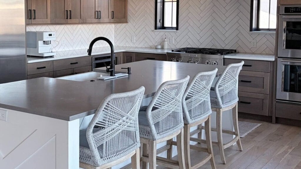 Counter stools with gray quartz countertop, wood cabinets, and chevron tile backsplash