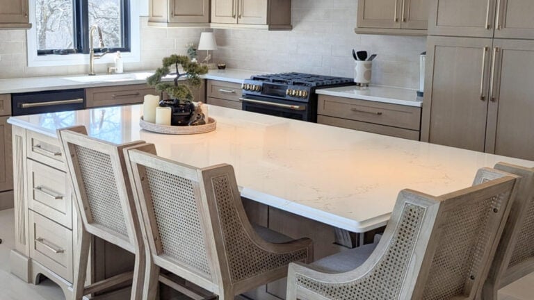 Whitewashed stained wood kitchen cabinets with bar stools and MIsterio Gold quartz countertop