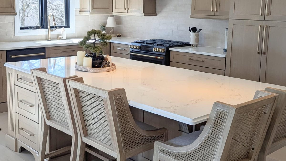 Whitewashed stained wood kitchen cabinets with bar stools and MIsterio Gold quartz countertop
